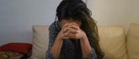 Woman sits on a sofa with her head in her hands